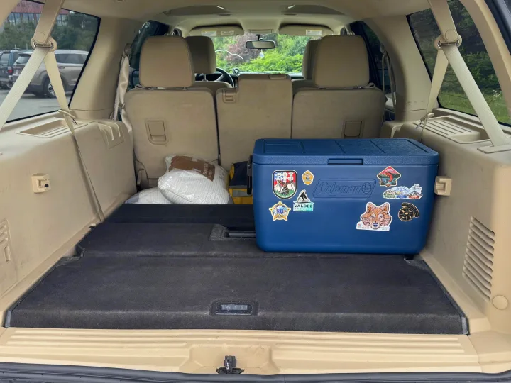 Rear cargo of an RV rental SUV, packed with a Coleman cooler, Alaska stickers, and pillows. Seats folded for road trip storage.. Ford Explorer 2016