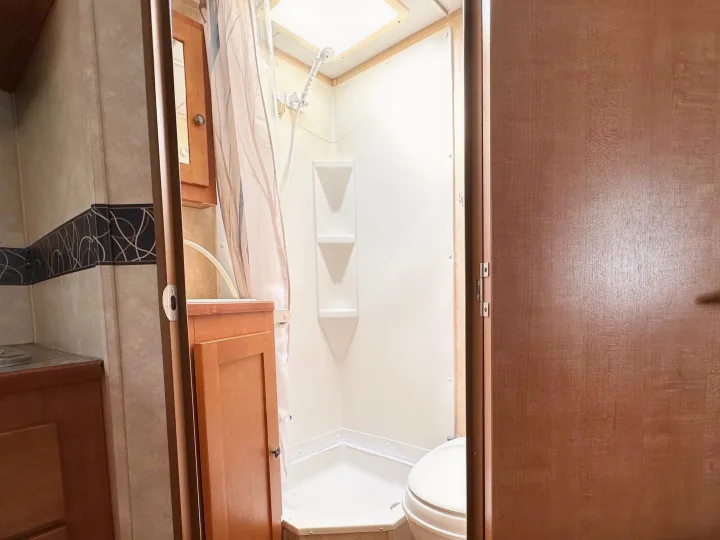 Inside a clean RV rental bathroom, featuring a white shower stall with corner shelves, a toilet, and a compact vanity area.. Cruiser RV Fun Finder X 2011