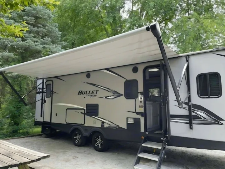 Bullet travel trailer RV rental at a green campsite, awning extended for shade.. Keystone RV Bullet Ultra Lite 2021