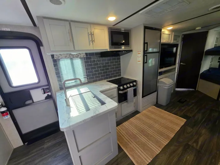 Spacious RV rental kitchen with modern light cabinets, dark floors, and full amenities, perfect for road trips.. Keystone RV Bullet Ultra Lite 2021