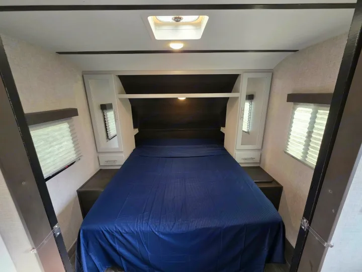 RV rental bedroom: cozy space with a large bed, headboard storage, and windows. Ideal for comfortable travel.. Keystone RV Bullet Ultra Lite 2021