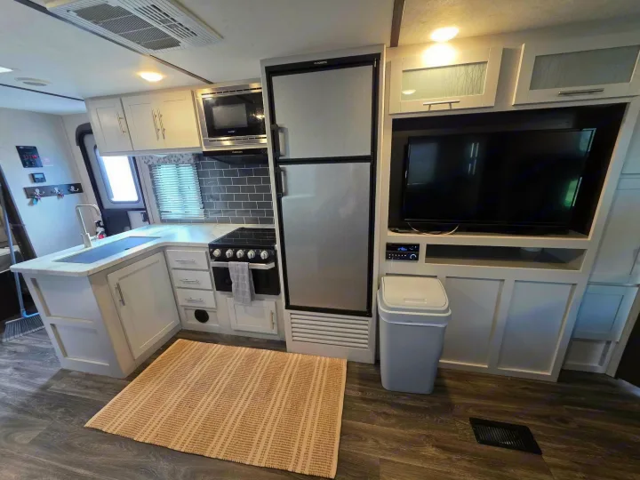 Modern RV rental kitchen & living area features a full fridge, microwave, and TV. Bright, clean interior for comfortable travel.. Keystone RV Bullet Ultra Lite 2021