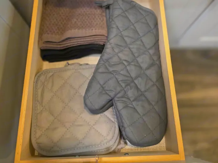 A tidy kitchen drawer in an RV rental, neatly organized with grey quilted oven mitts, a matching pot holder, and folded towels.. Keystone RV Bullet Ultra Lite 2021