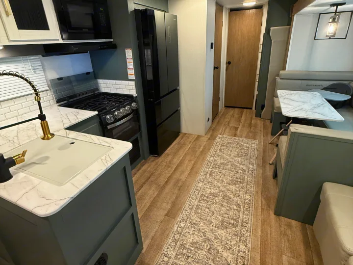 Modern RV rental interior: dark green kitchen, marble counters, wood floors, and a cozy dining booth with runner rug.. Heartland RVs Eddie Bauer 2026