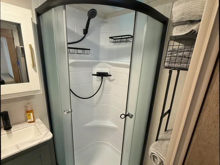 Modern RV rental bathroom featuring a compact shower with frosted glass doors, a sink vanity, and convenient towel storage.. Heartland RVs Eddie Bauer 2026