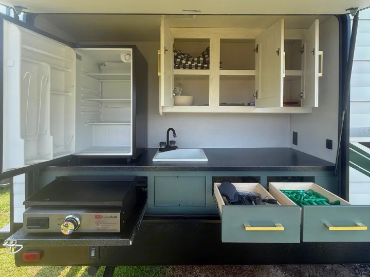 RV rental outdoor kitchen featuring an open fridge, sink, Suburban griddle, and accessible cabinets/drawers for convenience.. Heartland RVs Eddie Bauer 2026