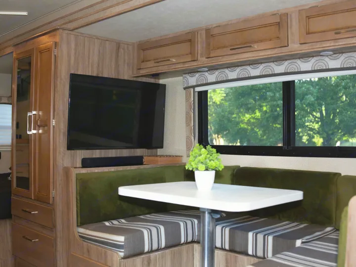 This RV rental interior features a cozy dinette with green cushions, a table, TV, and cabinets, offering a comfortable living space.. Entegra Coach Odyssey 2020
