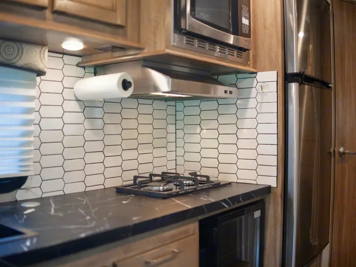 Modern RV rental kitchen with black countertops, hexagonal tile backsplash, and stainless steel appliances. Perfect for travel adventures.. Entegra Coach Odyssey 2020