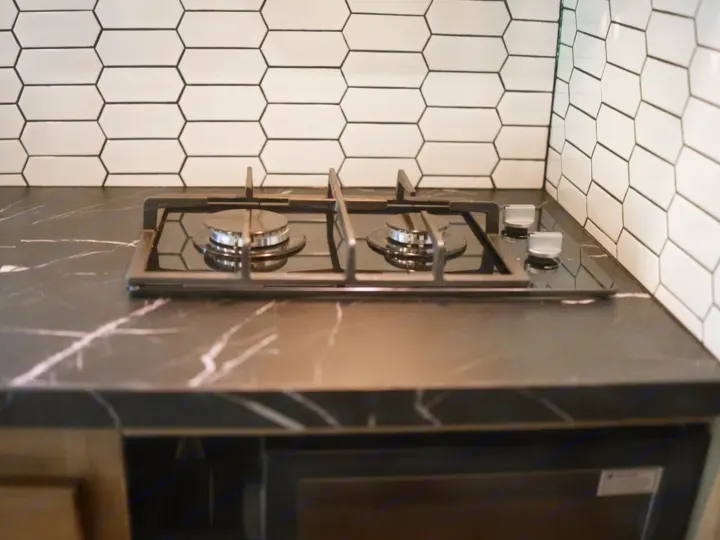 Modern RV rental kitchen featuring a sleek black gas stove, marble-look countertop, and white hexagonal tile backsplash.. Entegra Coach Odyssey 2020