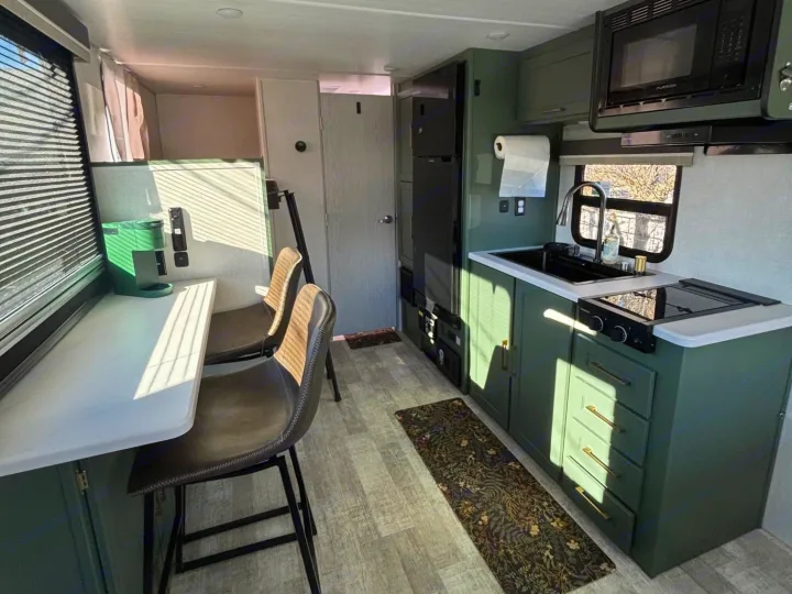 Inside a stylish rv rental: compact green kitchen, dining counter, & comfy seating for adventures.. No Boundaries 18 2025
