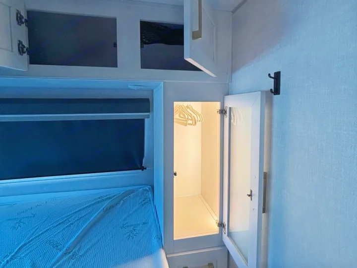 Compact RV rental bedroom showing a bamboo mattress, overhead cabinets, and an illuminated wardrobe for efficient storage.. No Boundaries 18 2025
