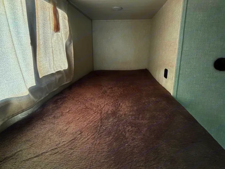 Cozy RV rental bunk bed: a compact sleeping space with dark gray bedspread, light walls, and window with sheer curtains.. No Boundaries 18 2025