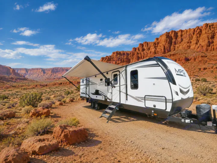 This RV rental, a white and black travel trailer, is parked in a vast desert landscape with stunning red rock canyons.. Cruiser RV MPG Ultra Lite 2021