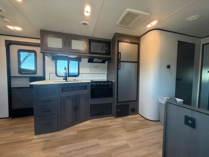 A modern RV rental kitchen area features dark cabinets, light countertops, a fridge, stove, microwave, and wood-look floors.. Cruiser RV MPG Ultra Lite 2021