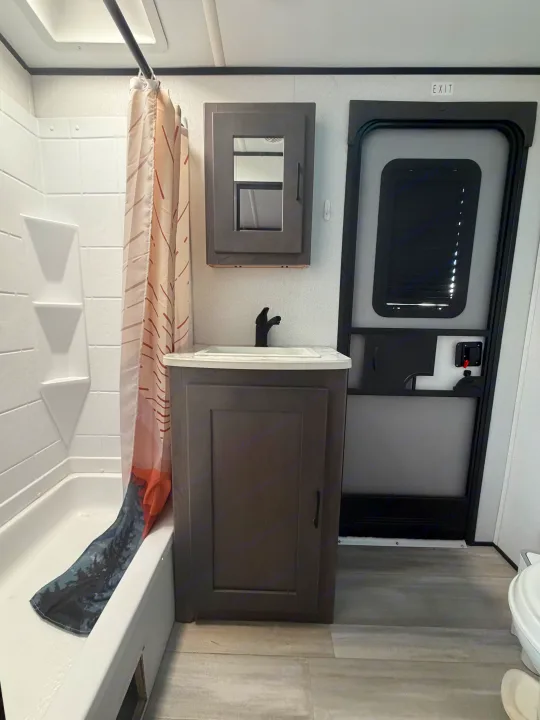 Inside an RV rental bathroom: a shower with landscape curtain, vanity with black faucet, mirrored cabinet, and exit door.. Cruiser RV MPG Ultra Lite 2021