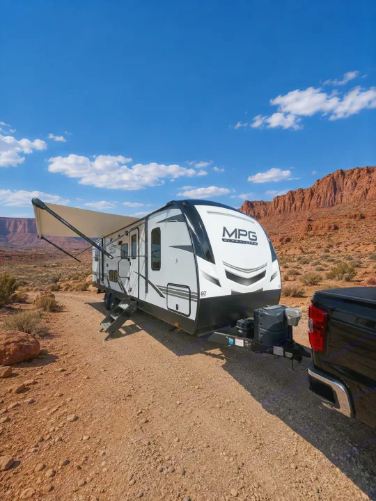 Explore the desert! This RV rental features a travel trailer with awning, hitched to a truck on a dirt road by red mountains.. Cruiser RV MPG Ultra Lite 2021