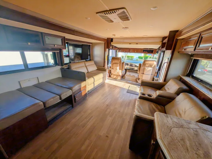 Spacious RV rental interior: wood floors, comfortable seating, TV, dinette, and cockpit with an overhead drop-down bed.. Holiday Rambler Admiral 2019