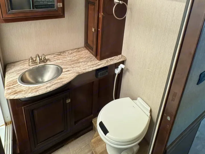 RV rental bathroom with vanity, stainless steel sink, mirror, toilet, and dark wood storage cabinets.. Holiday Rambler Admiral 2019