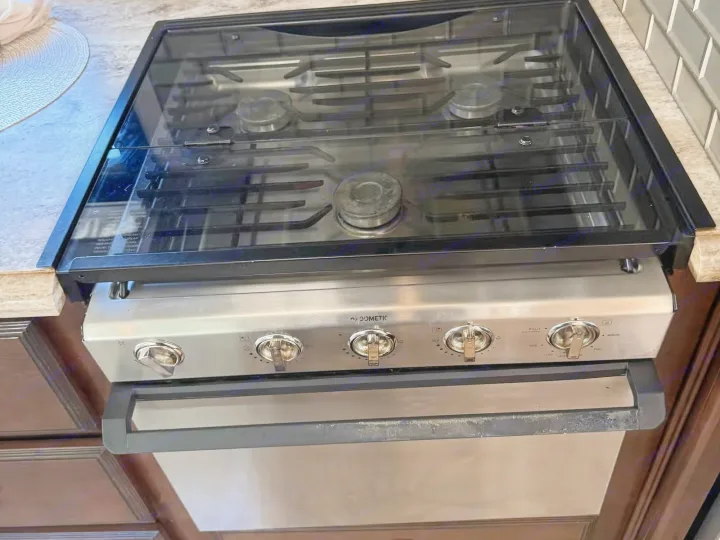 RV rental kitchen: modern Dometic stainless steel stove, oven, and glass cooktop with subway tile backsplash.. Holiday Rambler Admiral 2019