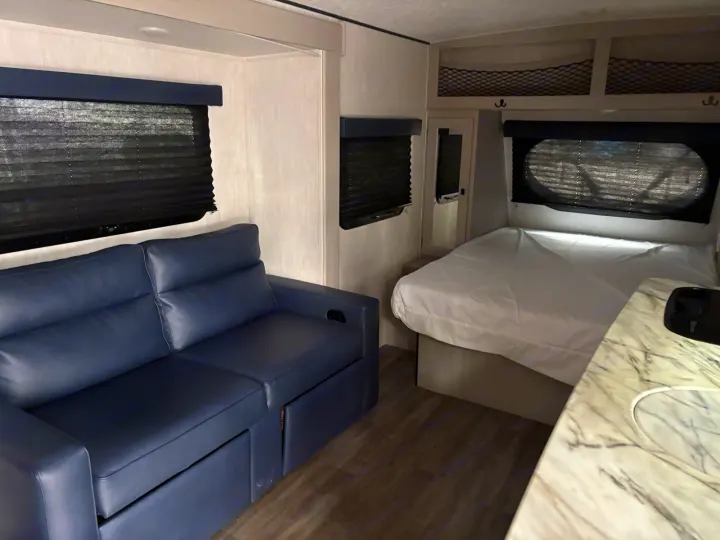 Relax in this rv rental's interior, featuring a blue sofa, cozy bed with white linens, and practical counter space.. Coachmen Other 2024