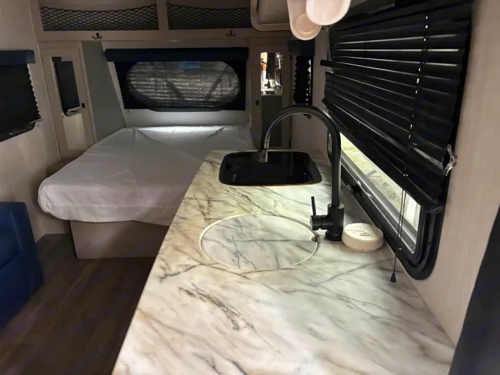 Modern rv rental interior: sleek kitchen counter with black sink, comfortable bed, and dark blinds for privacy and relaxation.. Coachmen Other 2024