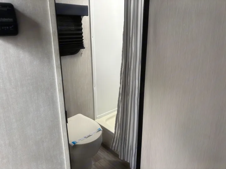 Inside an RV rental: compact bathroom featuring a sanitized toilet, striped shower, and Suburban thermostat.. Coachmen Other 2024