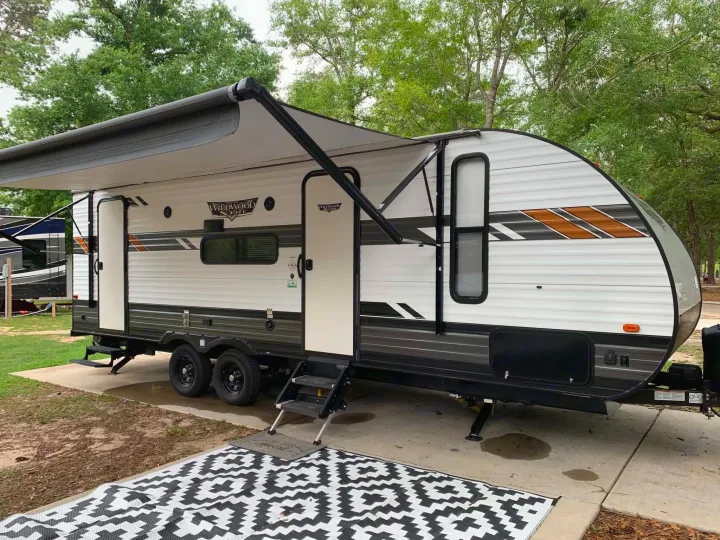 Travel trailer RV rental at a scenic campsite with an extended awning and outdoor rug for comfy outdoor living.. Forest River Wildwood X-Lite 2020