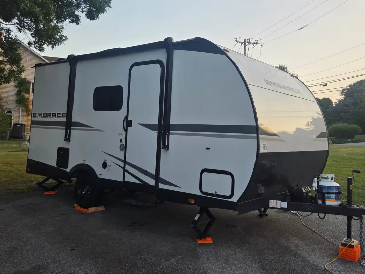 White and black Embrace travel trailer RV rental parked on a driveway, stabilized with blocks and propane tanks visible.. Cruiser RV Embrace 2025