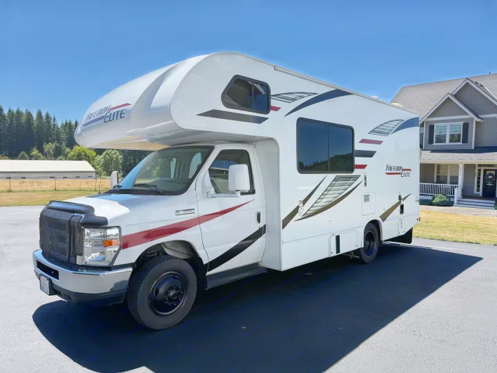 A white Freedom Elite Class C RV rental, with red and black stripes, parked on a sunny day. Ready for your next trip!. Thor Freedom Elite 2020