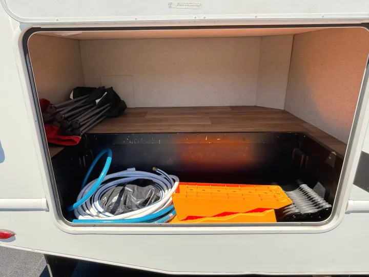 Inside an RV rental's exterior storage: essential camping gear like chairs, water hoses, leveling blocks, and wheel chocks.. Thor Freedom Elite 2020