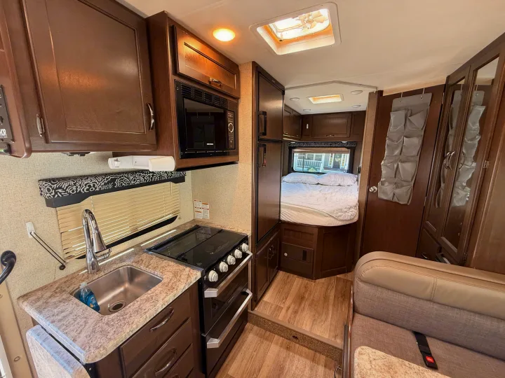 Interior of an rv rental showing a functional kitchen with sink, stove, microwave, sleeping area with bed, and dinette seating.. Thor Freedom Elite 2020