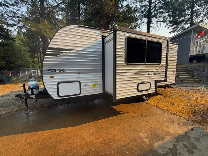 RV rental: A sleek SLX Baja Edition travel trailer parked on a concrete pad, gleaming with recent moisture, surrounded by trees.. Jayco Jay Flight SLX 2026