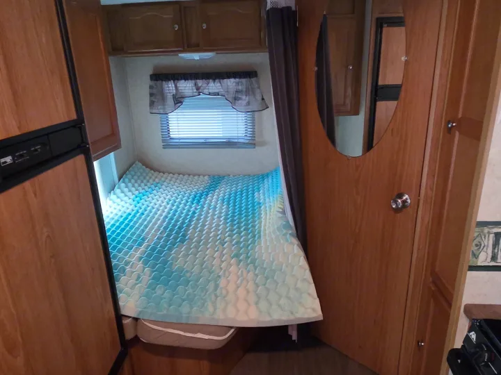 rv rental: A cozy camper bedroom with a bed featuring a blue-and-white wavy topper, window, wooden cabinets, and a fridge.. R-Vision Trail-Lite Trail-Cruiser 2007