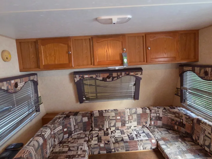 This RV rental living space features a patterned U-shaped sofa, wood cabinets, and two windows with blinds.. R-Vision Trail-Lite Trail-Cruiser 2007