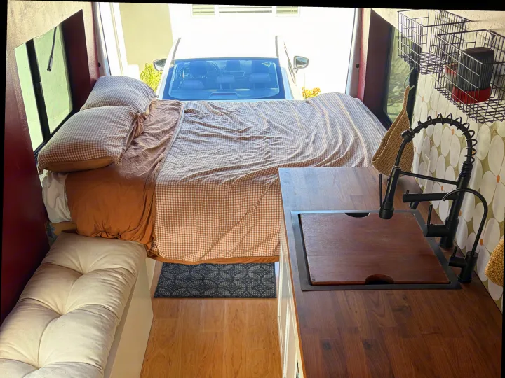 Cozy rv rental interior with a bed, kitchen counter, and sink, showing wood floors and patterned backsplash.. Ford Transit 2021