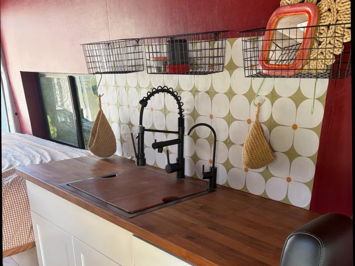 Functional RV rental kitchen: wood counters, modern black faucets, floral backsplash, and practical storage baskets.. Ford Transit 2021