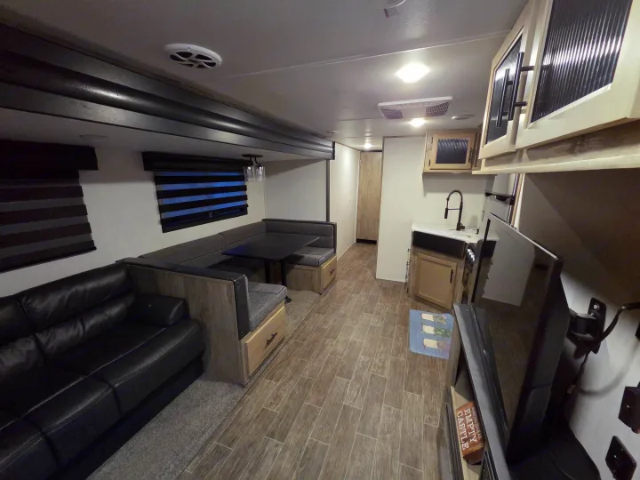 Inside a modern rv rental: a cozy living space with a black sofa, dinette, wood-look flooring, and a kitchen area.. Forest River Cherokee Alpha Wolf 2022