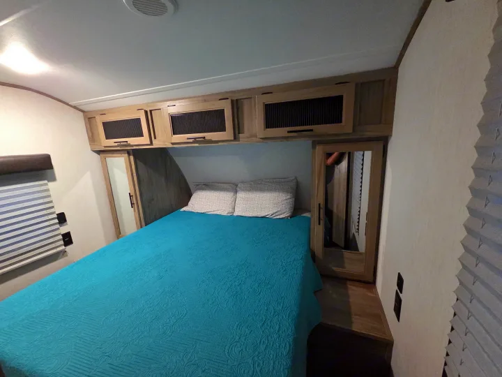 Cozy RV rental bedroom featuring a blue bedspread, overhead storage, and mirrored closets for a comfortable stay.. Forest River Cherokee Alpha Wolf 2022