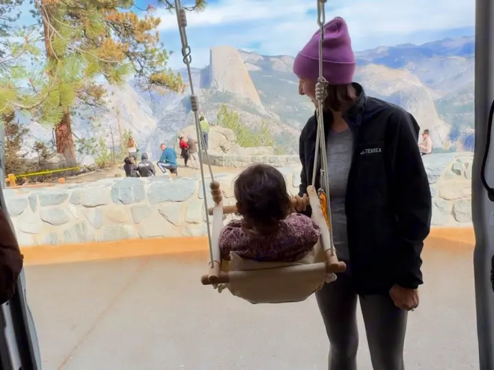 Stunning Yosemite views from our RV rental. A child in an indoor swing enjoys Half Dome, with a parent nearby.. Ford Transit 2021