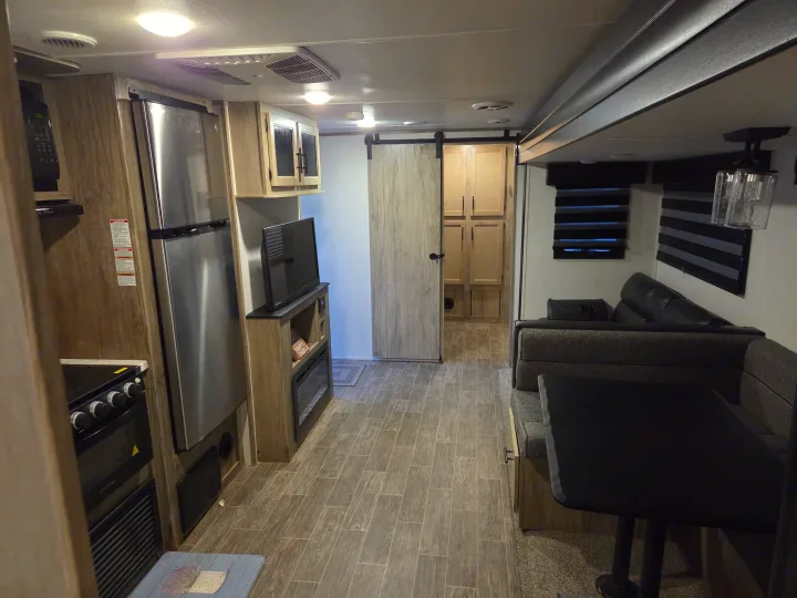 This modern RV rental interior features a kitchen with appliances, a dining booth, TV, and a barn door leading to more space.. Forest River Cherokee Alpha Wolf 2022