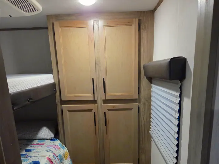 RV rental interior: bunk beds with bedding, light wood storage cabinets, and a window with blinds. Functional and compact.. Forest River Cherokee Alpha Wolf 2022