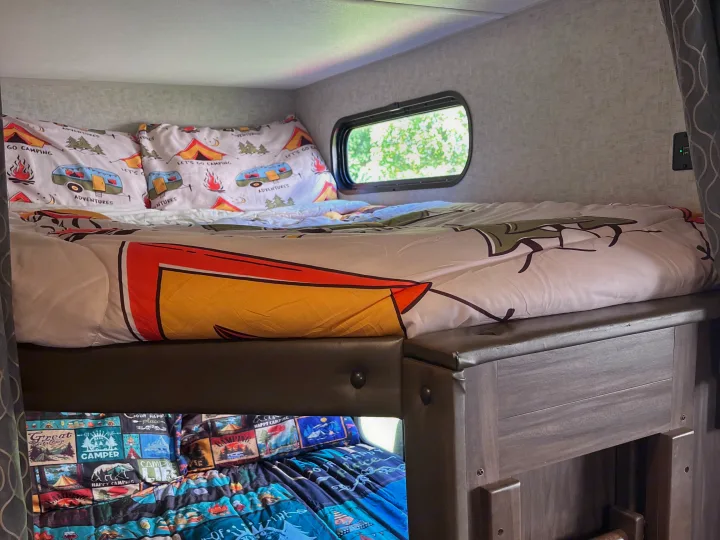 Cozy RV rental bunk beds featuring camping-themed bedding and a small window, providing comfortable accommodations for adventures.. Forest River Cherokee Grey Wolf 2018