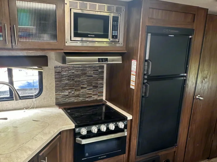 Well-equipped RV rental kitchen featuring microwave, Dometic fridge, Furrion range/oven, and sink. Ready for your travels!. Forest River Cherokee Grey Wolf 2018