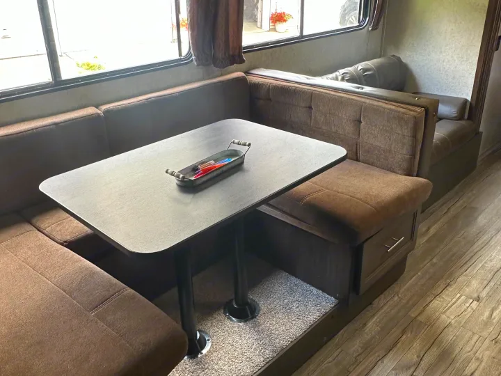 Modern RV rental dinette featuring a grey table, brown upholstered benches, and large windows. Ideal for travel comfort.. Forest River Cherokee Grey Wolf 2018