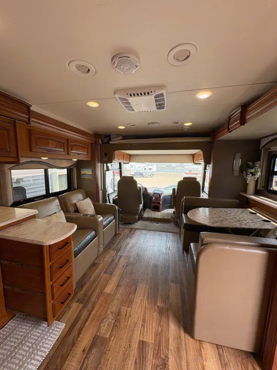Spacious RV rental interior featuring wood-look floors, comfy beige seating, wood cabinetry, and a view of the cockpit.. Jayco Precept 2017