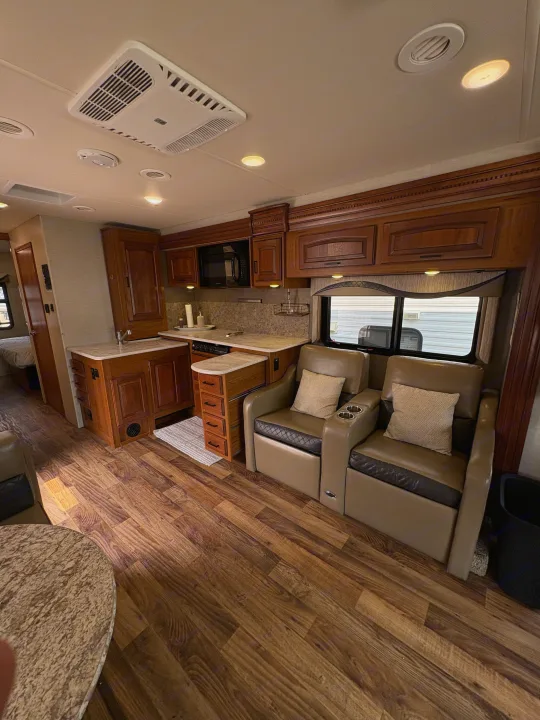 RV rental interior: spacious living area with full kitchen, warm wood cabinetry, comfortable recliners, and wood-look floors.. Jayco Precept 2017