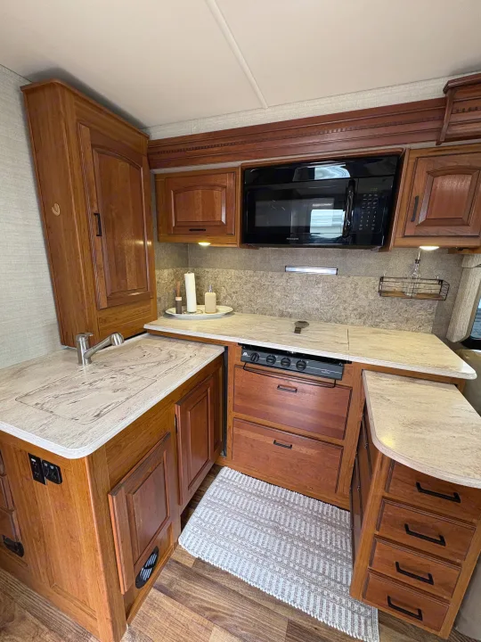 Modern RV rental kitchen featuring wood cabinets, light countertops, sink, microwave, and stovetop. Ready for your adventure!. Jayco Precept 2017