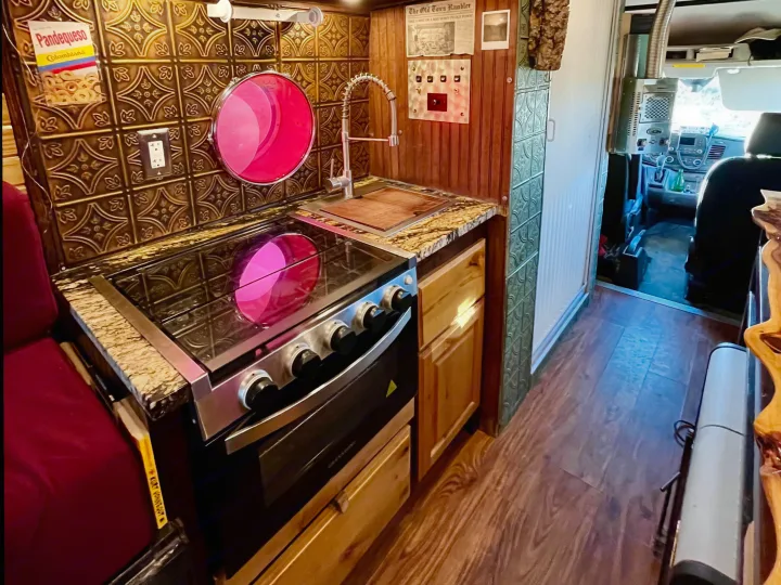 Stylish rv rental featuring a warm wooden kitchen with stove, sink, granite counter, and decorative backsplash.. Ford Transit 350 High Roof EXT 2020