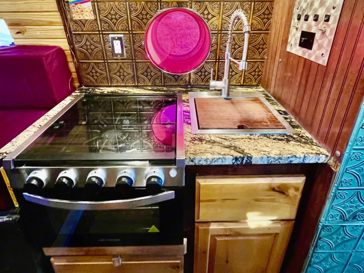 Inside a stylish RV rental: full kitchen with a stove, sink, wood cabinets & decorative backsplash.. Ford Transit 350 High Roof EXT 2020