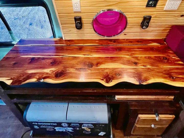 RV rental interior: custom wood walls, live-edge counter, Dometic fridge, electronics, and a distinctive pink drum.. Ford Transit 350 High Roof EXT 2020